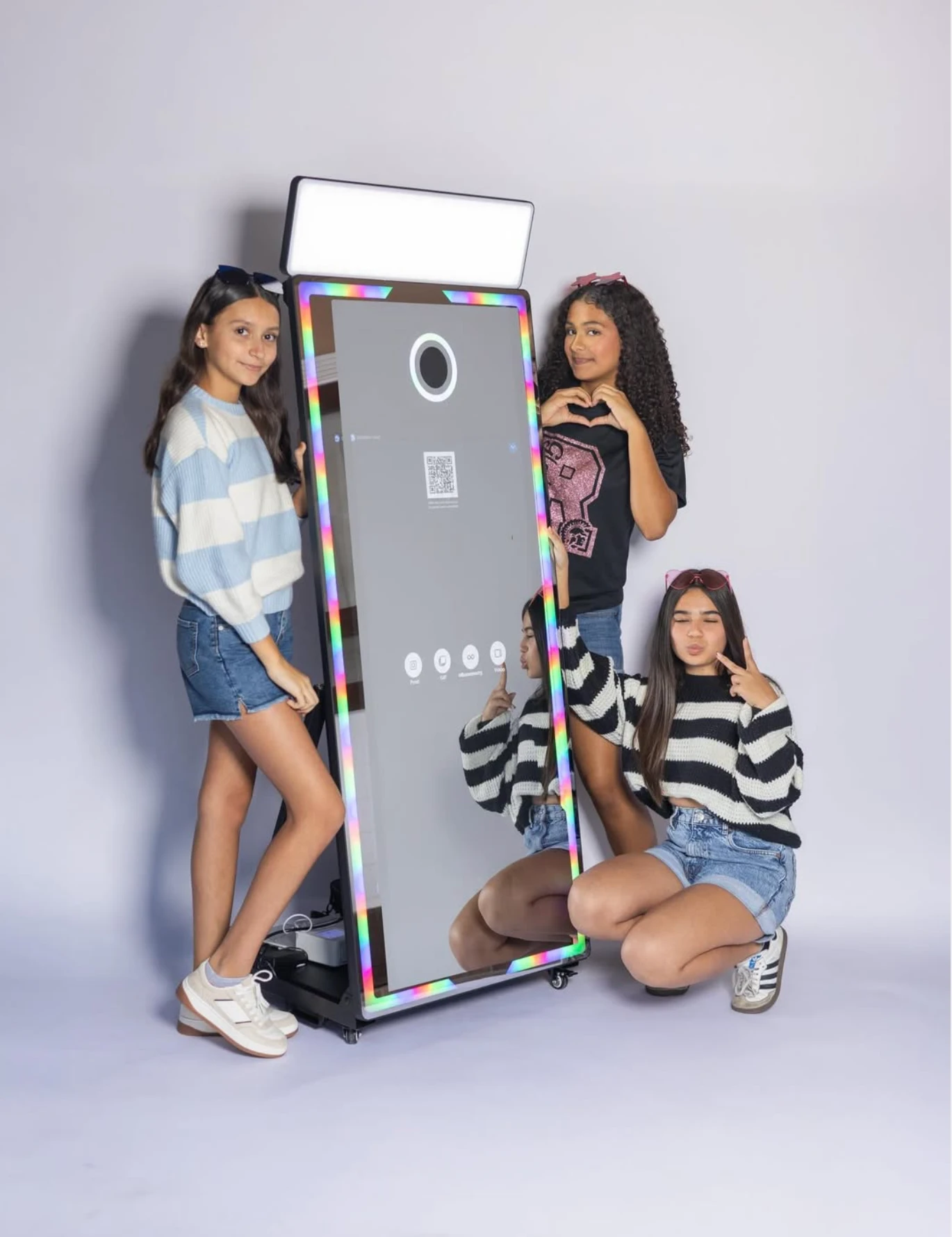Tres chavas posando junto al photobooth de espejo con luces de colores