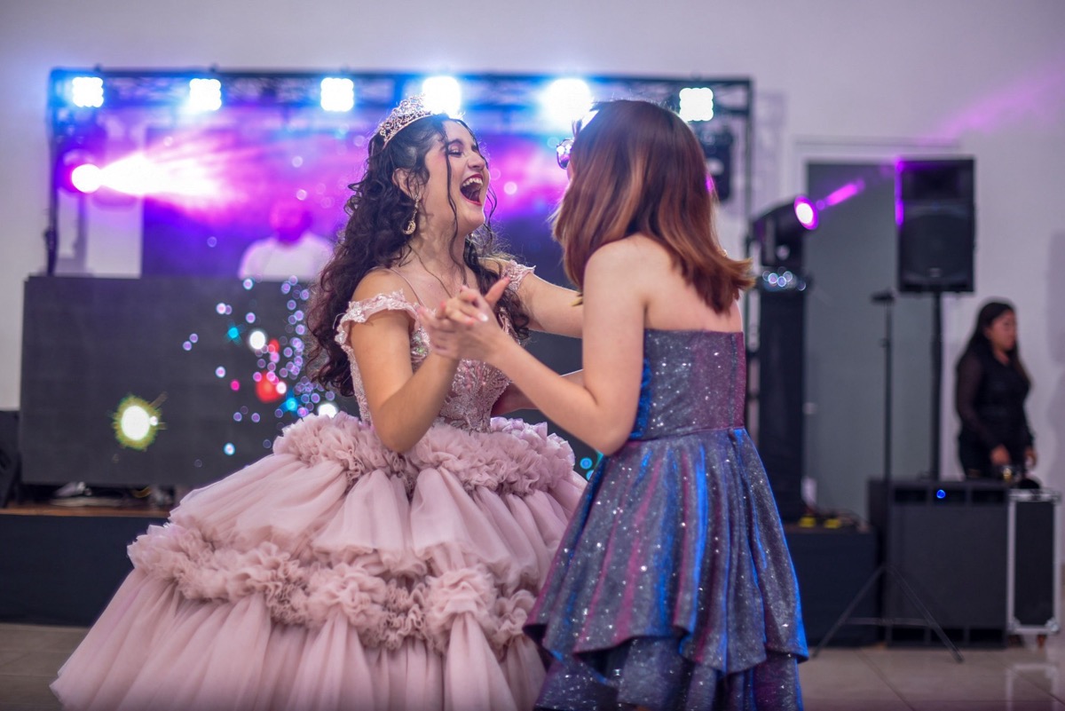 La quinceañera con corona y vestido rosa se ríe mientras baila con una amiga