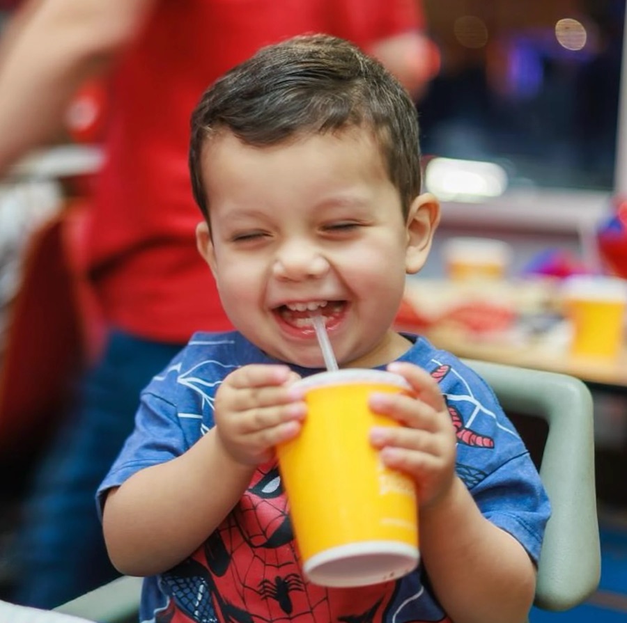 Niño con camisa de Spider-Man muerto de risa con su vaso de jugo
